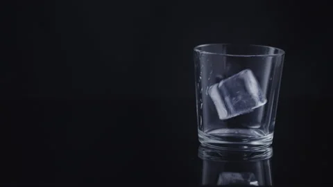 Closeup in a glass with ice cube pour whiskey on a black background Stock Footage 131065151