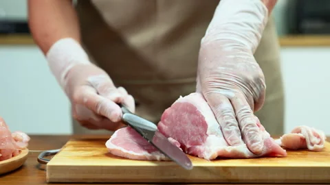 Closeup of a gloved hand slicing raw pork loin on a wooden board in a clean.. Video stock 312979646