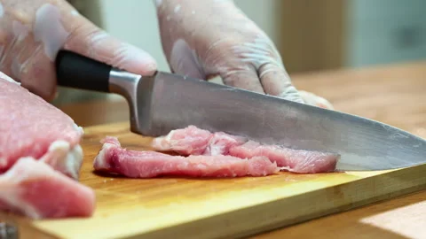 Closeup of a gloved hand slicing raw pork loin on a wooden board in a clean.. Stock Footage 312980067