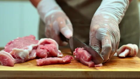 Closeup of a gloved hand slicing raw pork loin on a wooden board in a clean.. Stock Footage 312980141