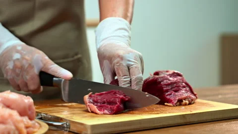 Closeup of gloved hands slicing raw beef steak on a wooden board. Ideal for.. Stock Footage 312980232