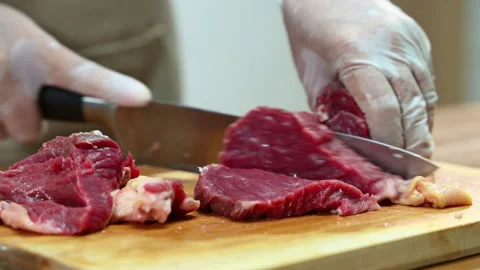 Closeup of gloved hands slicing raw beef steak on a wooden board. Ideal for.. Stock Footage 312980278