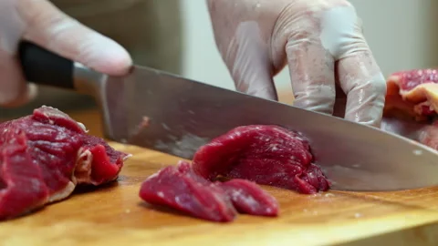 Closeup of gloved hands slicing raw beef steak on a wooden board. Ideal for.. Stock Footage 312980355