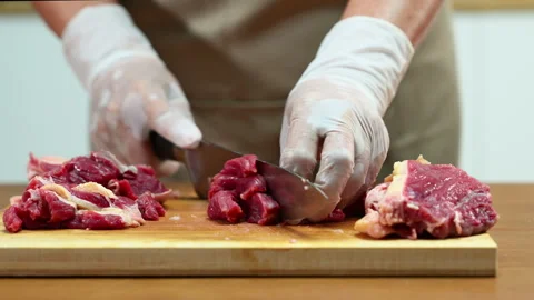 Closeup of gloved hands slicing raw beef steak on a wooden board. Ideal for.. Stock Footage 312980373