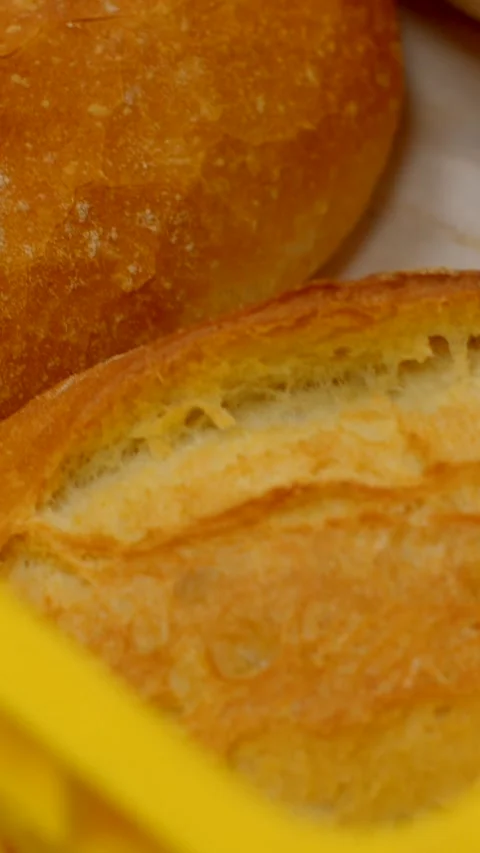 Closeup of golden crust bread loaves resting in yellow basket rim container Stock Footage 345601226