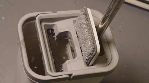 Closeup of a gray flat mop being wrung out in a self-cleaning bucket on a light Stock Footage 327682814