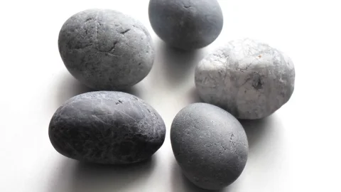 Closeup gray round stones spin on a light gray background. Ordinary plain Stock Footage 121564560