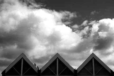 Closeup greyscale of triangle shape roofs under a cloudy sky Stock Photos