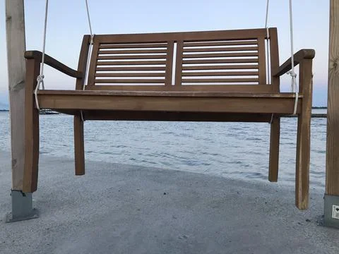 Closeup ground perspective of vacant double rocking bench on the pier with the s Stock Photos