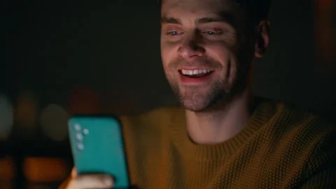 Closeup guy holding smartphone in night home. Smiling man reading cellphone Stock Footage 340116687