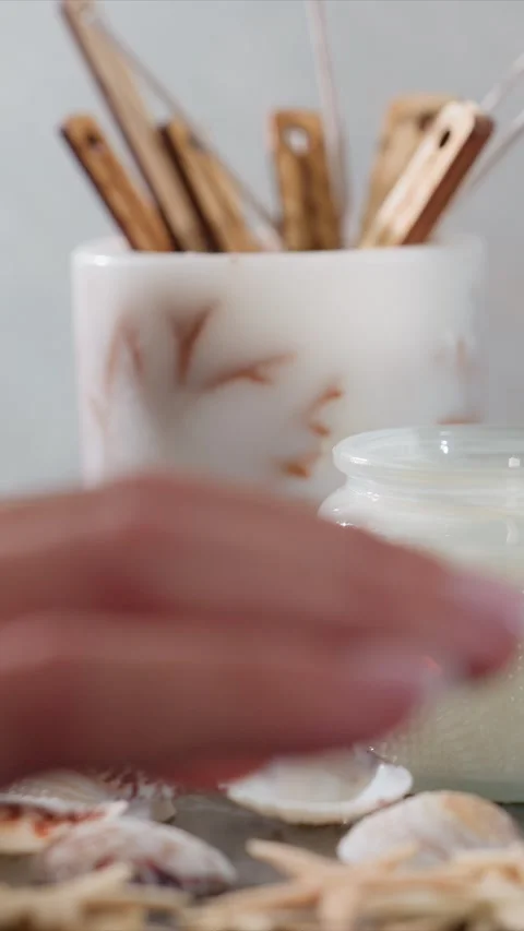 Closeup of hand arranging seashells on table with white candles and wooden craft Stock Footage 344682607
