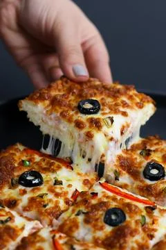 Closeup of a hand dipping a thick square pizza slice into rich red sauce Stock Photos