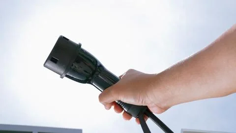 Closeup hand grasping an EV plug for electric vehicle as progressive idea. Stock Photos