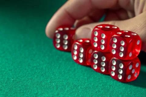 Closeup of hand holding red dice with a winning combination on green cloth in Stock Photos