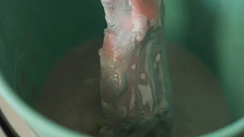 Closeup hand mixing gray clay slip in pottery workshop bucket, wet texture and Stock Footage 337363092