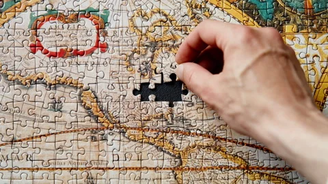 Closeup hand placing puzzle piece in vintage world map. Historical landscape Stock Footage 332310196