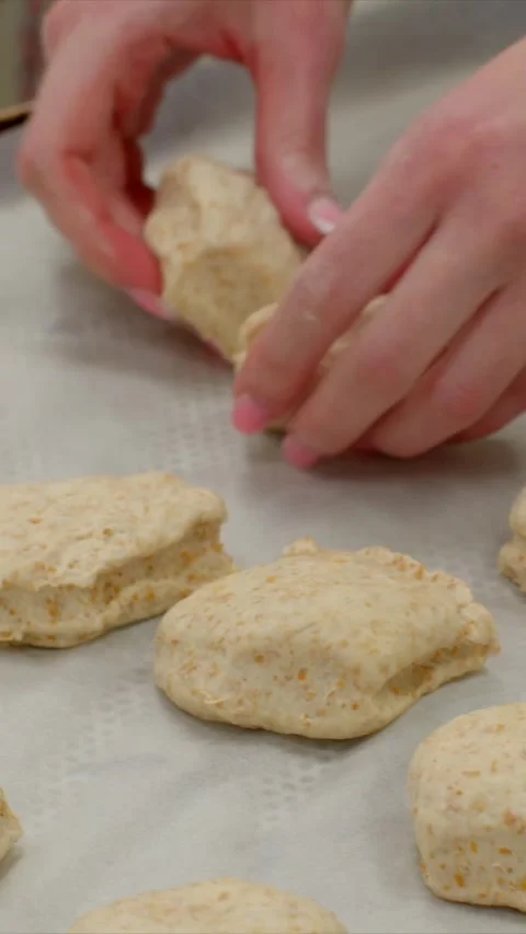 Closeup hand placing raw biscuit rounds on parchment-lined tray in bakery prep Stock Footage 345601512