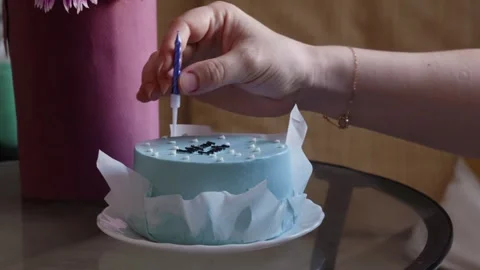 Closeup of hand putting candle on blue cake indoors, festive detail Stock Footage 318215410