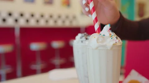 Closeup of hand putting paper drinking straw in milkshakes with whipped cream in Stock-Footage 209791443