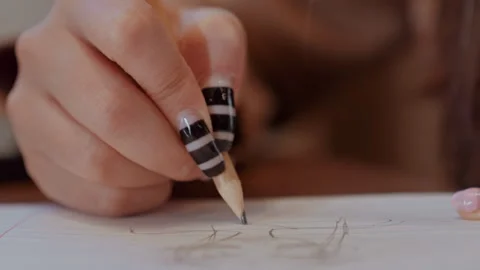 Closeup hand sketching pencil lines on paper, striped manicure visible, student Stock Footage 335889415