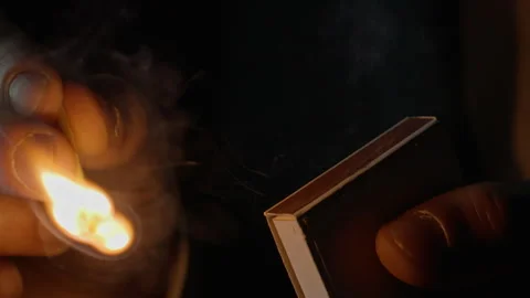 Closeup hand striking match using box edge creating spark on black background Stock Footage 332507457