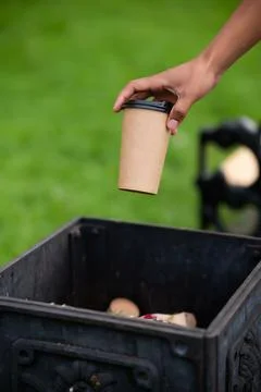 Closeup hand throwing empty paper disposable coffee cup in recycling bin. Eco Stock Photos