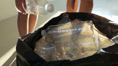 Closeup hand throwing plastic PET bottle into trash bag, slow motion Stock Footage 123959923