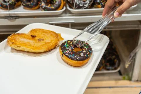 Closeup of hand using clamp picking donut at pastry shop Stock Photos