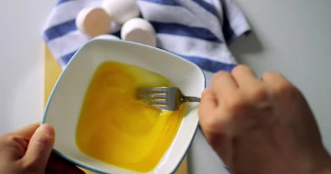 Closeup of hand whisking egg mixture in white bowl with fork, striped kitchen Stock Footage 315692943
