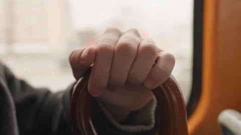 Closeup hand on wooden cane inside bus window wrapped coat sleeve, amber seat Stock Footage 345165488
