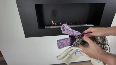 Closeup of hands adjusting crafted wool socks around gentle indoor heat source Stock Footage 321950984