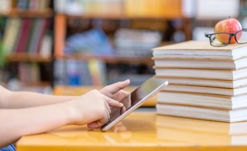 Closeup hands of a child use tablet computer in library. Empty space for text Stock Photos