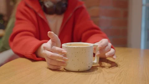 Closeup hands clasping mug at cafe cozy brick interior wooden table red sweater Stock Footage 345171810