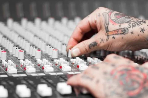 Closeup of hands covered with tattoos working on mixer console, twisting knobs Stockfoto's