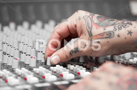 Closeup Of Hands Covered With Tattoos Working On Mixer Console, Twisting Knobs