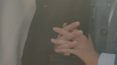 Closeup hands entwined over jacket, intimate gesture symbolizing commitment and Stock Footage 331533127