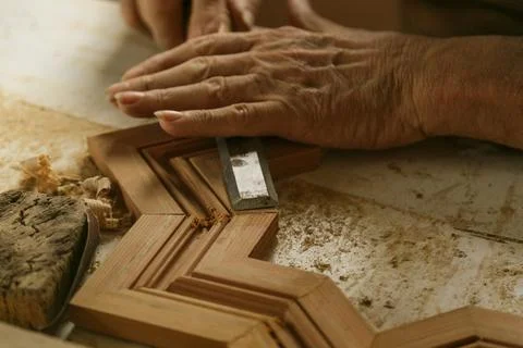 A closeup of hands expertly and skillfully carving intricate wooden frame det Stock Photos