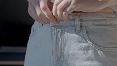Closeup of hands fastening button on light denim jeans at waist Stock Footage 330261796