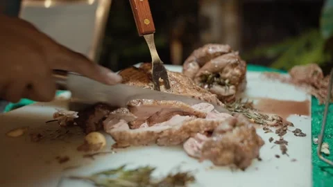 Closeup of hands holding a knife cutting smoked pork steak on a cutting board at Video stock 280871004