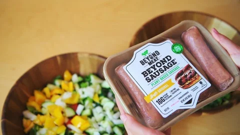 Closeup of hands holding raw beyond meat sausages package with salad bowls Stock Footage 111906326