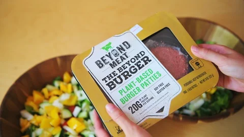 Closeup of hands holding raw beyond meat burger patties package with salad bowls Vidéo 111908443