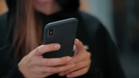 Closeup of hands of Modern teenager girl in a hood using a smart phone inside a Stock Footage 148779552