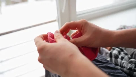 Closeup hands picking tiny infant socks from a laundry basket by a window. Cozy Video stock 327689869