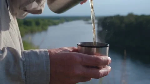 Closeup hands pouring hot drink mug from thermos on river bank. selective focus. Stock Footage 233447136