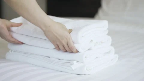 Closeup hands putting a stack of new clean bath towels on the bed Video stock 159861352
