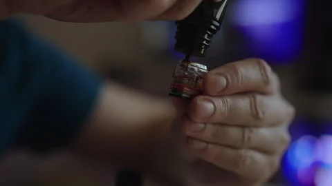 Closeup of hands refilling vape pod with e liquid from dropper bottle, detailed Stock Footage 342768940
