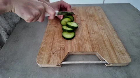 Closeup of hands skillfully slicing cucumber on wooden table Stock Footage 325199250