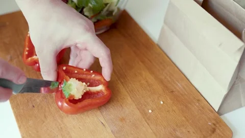 Closeup of hands slicing bell pepper and putting a waste into a paper trash bag. Video stock 305848878