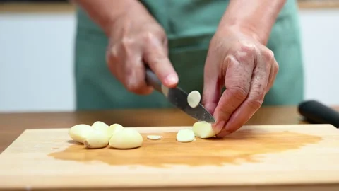 Closeup of hands slicing fresh garlic on a wooden cutting board in kitchen... Stock Footage 312979018