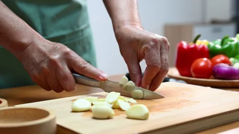 Closeup of hands slicing fresh garlic on a wooden cutting board in kitchen... Video stock 312979134